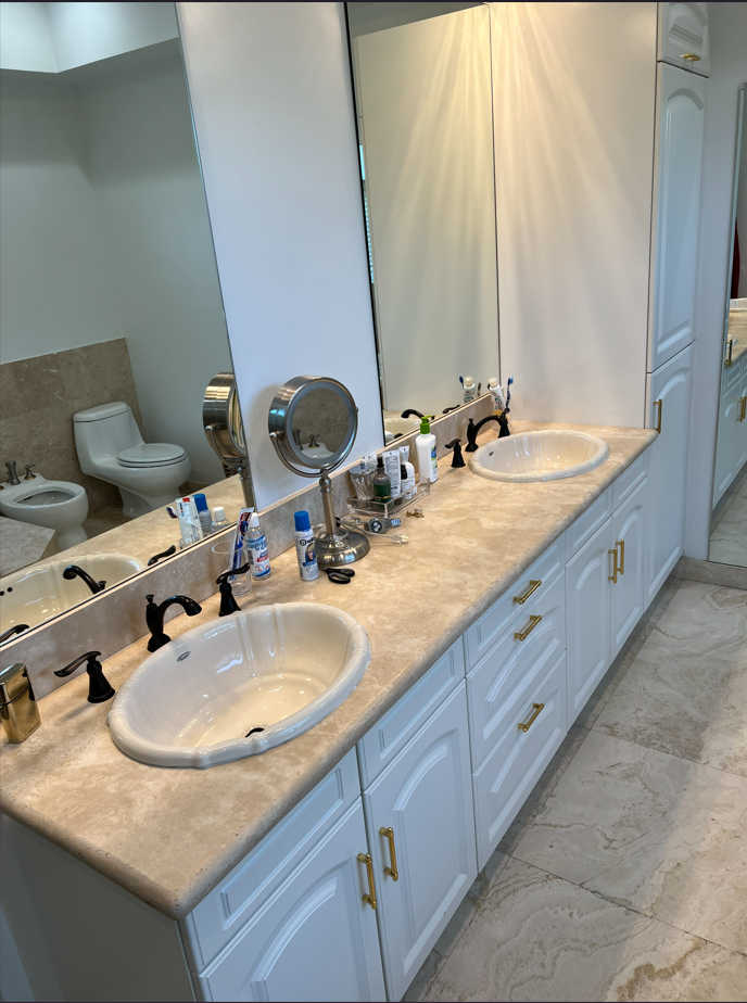 Dated bathroom with travertine counters and drop-in sinks before the repipe
