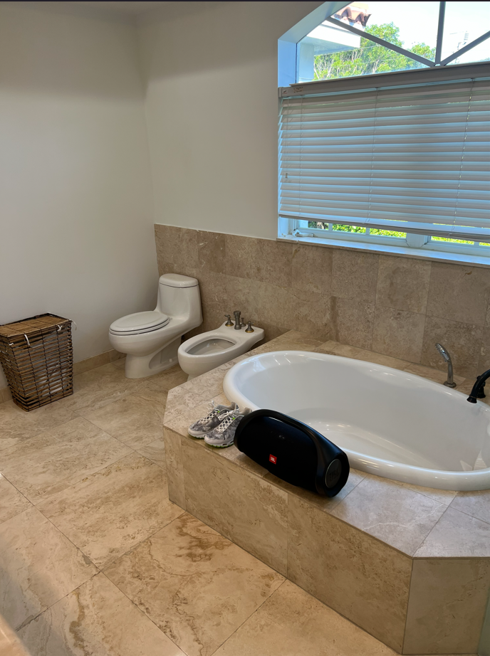 Dated bathroom with a built-in drop-in tub, toilet, and bidet on travertine tile